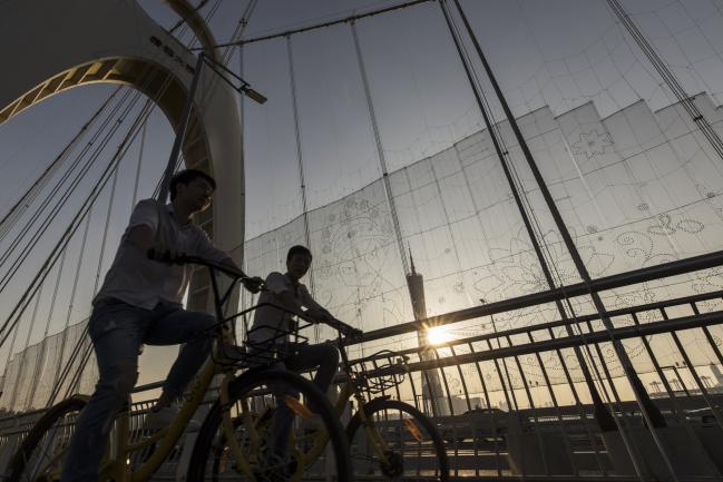 © Bloomberg. Cyclists ride Ofo Inc. bicycles on the Liede Bridge over the Pearl River in Guangzhou, China, on Wednesday, Nov. 1, 2017. China is poised for an acceleration of deals as confidence grows in the wake of last month’s Communist Party gathering and as the nation opens up to reforms.