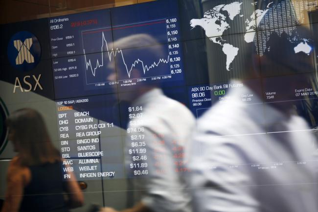 © Bloomberg. Pedestrians are reflected in a window as they walk past an electronic stock board at the ASX Ltd. exchange centre in Sydney, Australia, on Thursday, Feb. 14, 2019. “We made good progress on our core initiatives across the period, including the program to replace CHESS with distributed ledger technology; upgrade of our secondary data centre to strengthen market resilience; and restructure of our Listings Compliance team to enhance the quality of market oversight,” ASX Chief Executive Officer Dominic Stevens said. Photographer: David Moir/Bloomberg