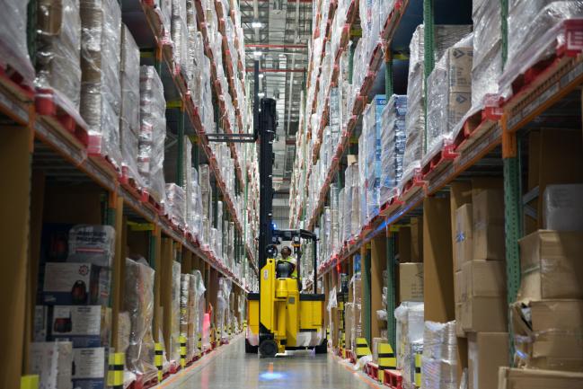 © Bloomberg. A worker uses a forklift to remove a pallet of goods from a storage rack in an aisle at the Amazon Inc. fulfillment center in Bengaluru, India. 