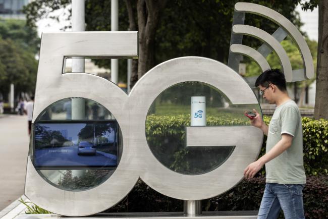 © Bloomberg. An employee using a smartphone walks past a sign for the 5G Park at the Huawei Technologies Co. headquarters in Shenzhen, China, on Wednesday, May 22, 2019. Huawei is seeking about $1 billion from a small group of lenders, its first major funding test after getting hit with U.S. curbs that threaten to cut off access to critical suppliers. 