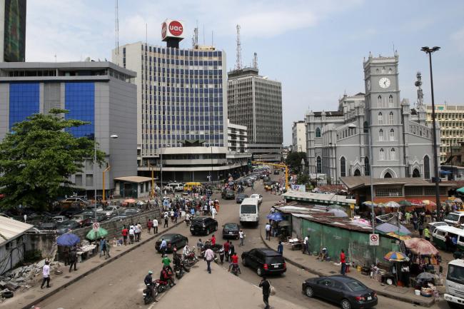 © Bloomberg. Pedestrians pass street traders in the business district of Lagos, Nigeria. Photographer: George Osodi