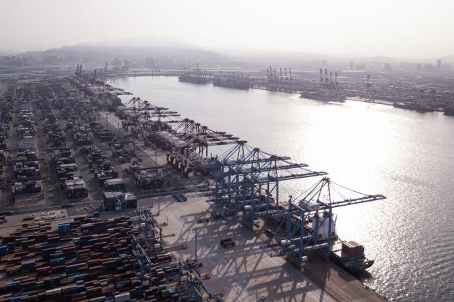 © Bloomberg. Cargo ships are moored under cranes as shipping containers stand at the Qingdao Qianwan Container Terminal in this aerial photograph taken in Qingdao, China, on Monday, May 7, 2018. China's overseas shipments exceeded estimates while imports surged, as the global economy continued to support demand. 