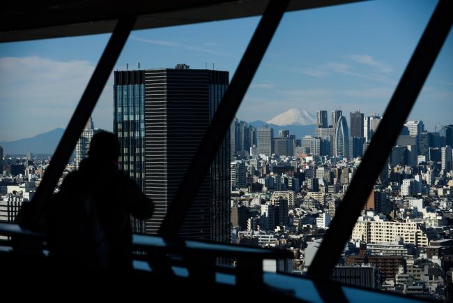 © Bloomberg. Mount Fuji stands beyond buildings as a visitor looks out at the skyline from an observation deck in Tokyo, Japan, on Friday, Jan. 11, 2019. Japan’s key inflation gauge slowed in the first back-to-back decline since April, highlighting the difficulty of the Bank of Japan’s price goal ahead of its policy meeting next week. Photographer: Akio Kon/Bloomberg