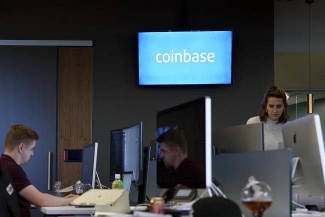 © Bloomberg. Signage is displayed on a monitor as employees work at the Coinbase Inc. office in San Francisco, California, U.S., on Friday, Dec. 1, 2017. Coinbase wants to use digital money to reinvent finance. In the company's version of the future, loans, venture capital, money transfers, accounts receivable and stock trading can all be done with electronic currency, using Coinbase instead of banks.