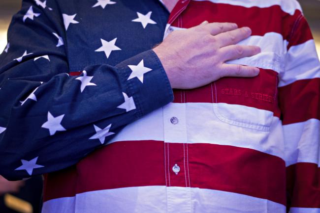 © Bloomberg. An attendee wearing an America flag shirt stands for the Pledge of Allegiance at the Conservative Political Action Conference (CPAC) in National Harbor, Maryland, U.S. 