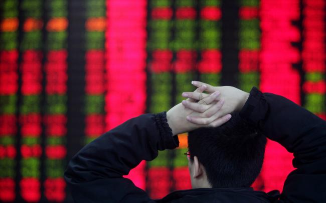 © Bloomberg. A customer watches share prices on an electronic stock board at a security firm in Shanghai, China. 