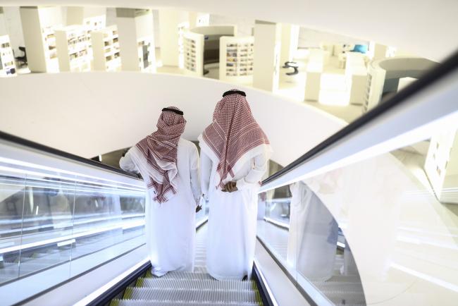 © Bloomberg. Attendees stand on an escalator as they move through the interior of the King Abdulaziz Center for World Culture during a tour of the project in Dhahran, Saudi Arabia, on Friday, Nov. 25, 2016. When completed, the project designed for the Saudi Arabian Oil Co. (Aramco) will contain diverse cultural facilities, including an auditorium, cinema, library, exhibition hall, museum and archive. 