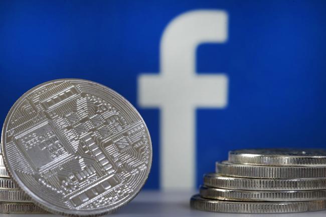 © Bloomberg. PARIS, FRANCE - JUNE 18: In this photo illustration, a visual representation of a digital cryptocurrency coin sits on display in front of a Facebook logo on June 17, 2019 in Paris, France. Facebook will announce Tuesday, June 18 the details of its cryptocurrency, called 