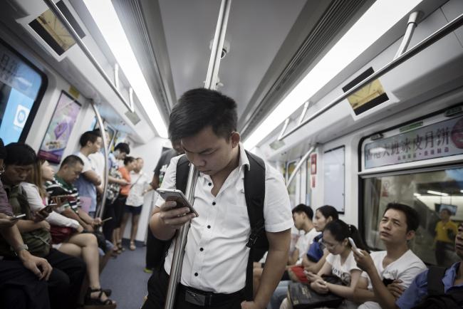 © Bloomberg. A passenger looks at a smartphone on a subway train in Shenzhen, China. Photographer:Qilai Shen/Bloomberg 