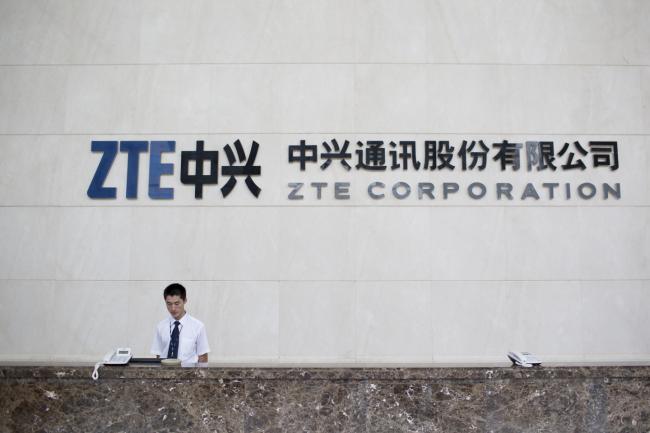 © Bloomberg. ZTE Corp. signage is displayed near an employee at the company's headquarters in the Nanshan district of Shenzhen, China, on Thursday, Aug. 7, 2014. Photographer: Brent Lewin