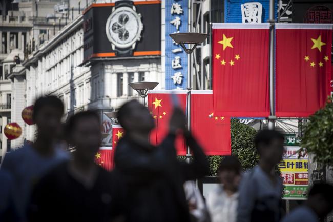 © Bloomberg. Pedestrians walk past Chinese national flags displayed along the Nanjing Road pedestrian street in Shanghai, China, on Friday, Oct. 2, 2015. China's consumer inflation moderated and factory gate deflation extended a record stretch of declines, signaling the People's Bank of China still has room to ease monetary policy further to support a slowing economy.