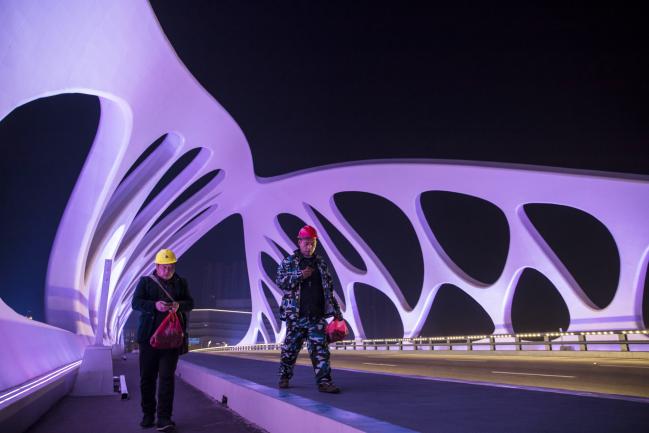 © Bloomberg. Workers walk across an illuminated bridge connecting Qingdao and the Dalian Wanda Group Co. Oriental Movie Metropolis film production hub at night in Qingdao, China, on Tuesday, April 17, 2018. Wanda, a real-estate, retail and entertainment conglomerate, is opening its doors to an audacious 50 billion yuan ($7.9 billion) world-class film production hub, called the Oriental Movie Metropolis, or Dong Fang Ying Du. 