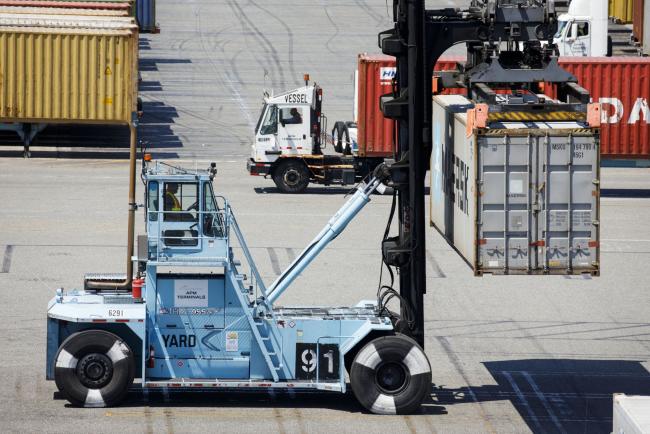 © Bloomberg. A worker operates a loaded container handler to move a shipping container at the APM shipping terminal in the Port of Los Angeles in Los Angeles, California, U.S., on Tuesday, May 7, 2019. The terminal is planning to replace diesel trucks and human workers. It has already ordered an electric, automated carrier from Finnish manufacturer Kalmar, part of the Cargotec Corp., that can fulfill the functions of three kinds of manned diesel vehicles: a crane, top-loader and truck. 