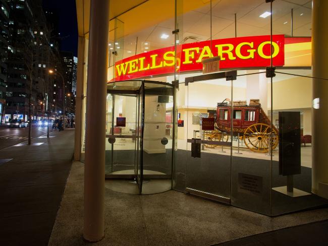 © Bloomberg. Pedestrians pass in front of a Wells Fargo & Co. bank branch at night in New York. 