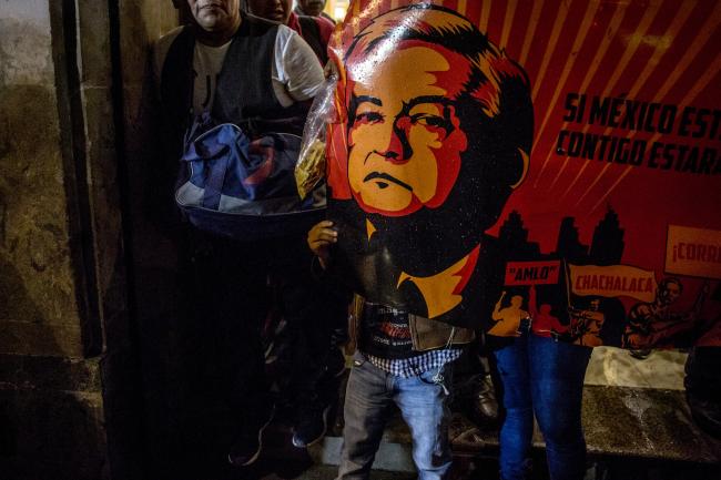 © Bloomberg. Supporters hold a sign displaying an image of Andres Manuel Lopez Obrador, presidential candidate of the National Regeneration Movement Party (MORENA), during the first presidential debate outside the Palace of Mining in Mexico City, Mexico, on Sunday, April 22, 2018. Mexico's peso, the world's best-performing currency this year, will probably depreciate as attention turns from Nafta optimism to political risks associated with presidential front-runner Lopez Obrador. Photographer: Alejandro Cegarra/Bloomberg