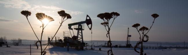 © Bloomberg. An oil pumping jack, also known as a 'nodding donkey,' operates in a snow covered oilfield near a derrick, right, during drilling operations in an oilfield operated by Bashneft PAO in the village of Otrada, 150kms from Ufa, Russia, on Saturday, March 5, 2016. Bashneft is an upstream and down stream oil & gas provider which explores, produces and refines its own oil and gas which it extracts from brownfield reserves in the Russian Federation.