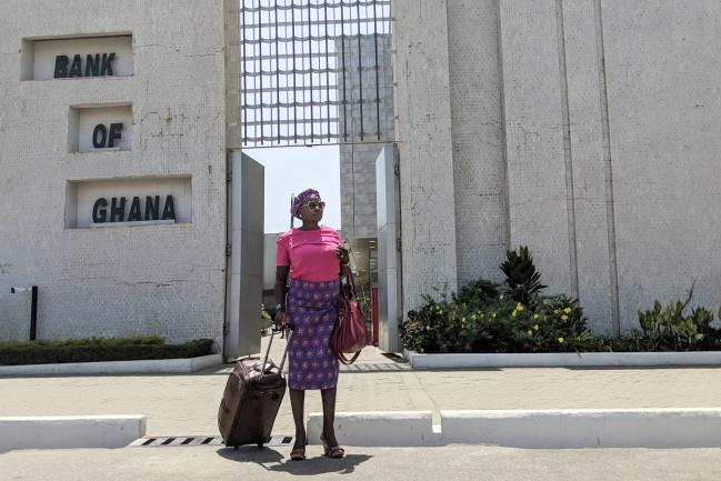 © Bloomberg. A pedestrian waits outside the headquarters of Ghana's central bank, also known as the Bank of Ghana, in Accra, Ghana, on Thursday, March 15, 2018. Ghana wants to shake up the way it collects tax with the International Monetary Fund telling the government that it’s not raising sufficient income. Photographer: Nicholas Seun Adatsi/Bloomberg