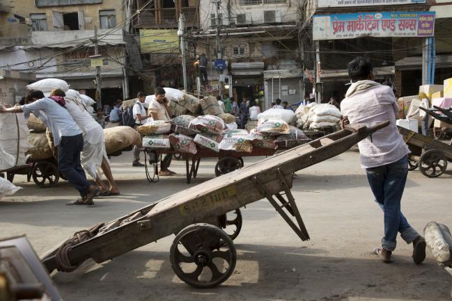 © Bloomberg. A worker leans against a cart as other workers transport goods at Khari Baoli spice market in New Delhi, India, on Wednesday, May 30, 2018.  Photographer: Ruhani Kaur/Bloomberg