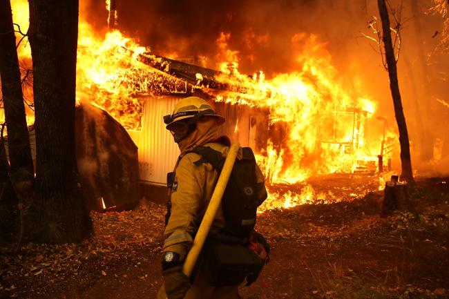 © Bloomberg. A Cal Fire firefighter monitors a burning home as the Camp Fire moves through the area on November 9, 2018 in Magalia, California. Photographer: Justin Sullivan/Getty Images North America