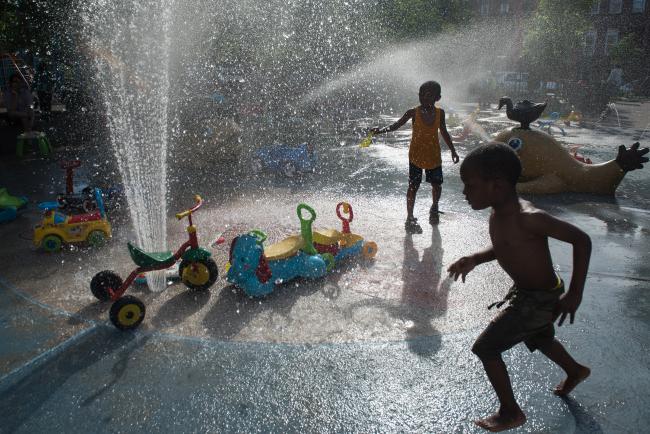 © Bloomberg. NEW YORK, NY - MAY 29: Children run through the sprinklers at a playground on May 29, 2016 in the Brooklyn borough of New York City. New York City is experiencing higher than average temperatures for the holiday weekend. (Photo by Stephanie Keith/Getty Images)