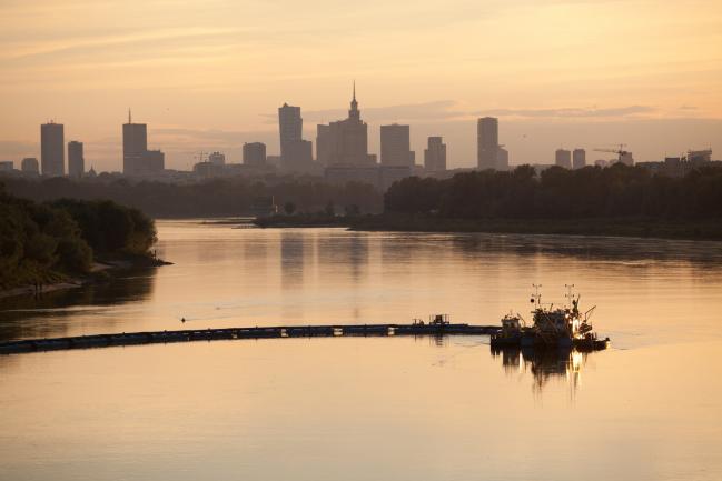 © Bloomberg. A dredger works on the River Vistula beyond the city skyline at dusk in Warsaw, Poland. 