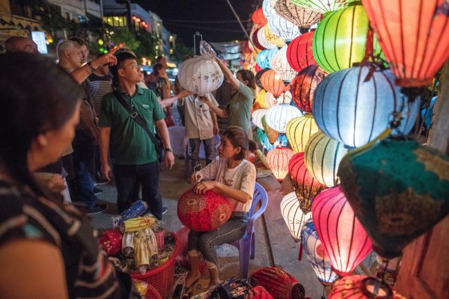 &copy Bloomberg. A vendor prepares a lantern at a street stall in the old town of Hoi An, Quảng Nam Province, Vietnam, on Sunday, April 22, 2018. With a fast-growing economy and a young population, Vietnam offers an attractive market for retailers. Its economy expanded 7.4 percent in the first quarter from the same period a year earlier, and a third of its population is aged 15 to 34. 