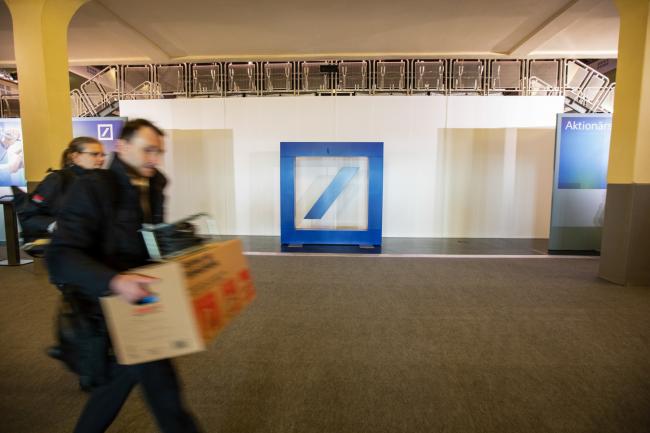 © Bloomberg. Workers carry boxes past a Deutsche Bank AG logo at the bank's annual general meeting in Frankfurt, Germany, on Thursday, May 23, 2019. Deutsche Bank’s leadership on Thursday will face investors exasperated by years of low profit and a falling share price. Photographer: Alex Kraus/Bloomberg