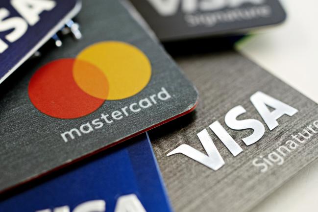 © Bloomberg. Visa Inc. and Mastercard Inc. credit cards are arranged for a photograph in Tiskilwa, Illinois, U.S., on Tuesday, Sept. 18, 2018. Visa and Mastercard agreed to pay as much as $6.2 billion to end a long-running price-fixing case brought by merchants over card fees, the largest-ever class action settlement of an antitrust case. 