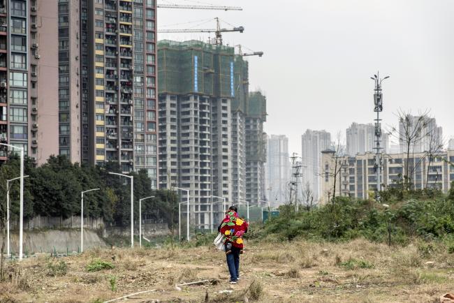 © Bloomberg. A man carrying a child on his back walks across a clearing past residential buildings on the outskirts of Chongqing, China, on Friday, Jan. 4, 2019. U.S. and Chinese officials began trade negotiations in the hope of reaching a deal during a 90-day truce between President Donald Trump and his counterpart Xi Jinping reached in early December. Photographer: Qilai Shen/Bloomberg