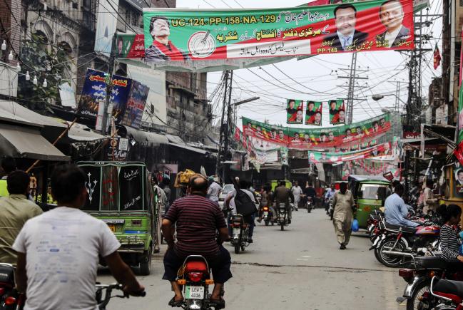 © Bloomberg. Traffic travels along a road past campaign banners for Pakistan Tehreek-e-Insaf (PTI), also known as Movement for Justice, in Lahore, Pakistan, on Thursday, July 17, 2018. Whoever wins Pakistan's election next week, gains in the rupee, stocks and bonds are likely to be short-lived as the new government grapples with a mounting set of economic challenges. Photographer: Asad Zaidi/Bloomberg