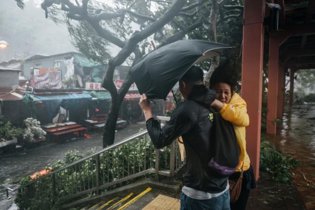 © Bloomberg. People hold an umbrella as they brave the wind during a No. 10 Hurricane Signal raised for Typhoon Mangkhut in Hong Kong, China, on Sunday, Sept. 16, 2018. Hong Kong issued its highest warning as a weakened though still dangerous Typhoon Mangkhut bears down on China's Guangdong province, after leaving a path of destruction across the northern Philippines. Photographer: Anthony Kwan/Bloomberg