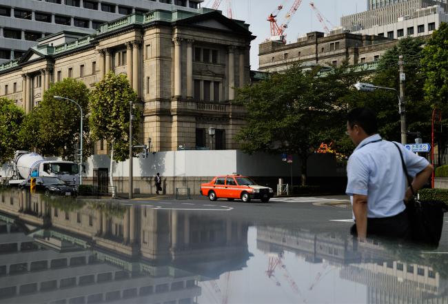 © Bloomberg. Pedestrians walk past the Bank of Japan (BOJ) headquarters in Tokyo, Japan, on Wednesday, Sept. 13, 2017. The BOJ's next monetary policy meeting is scheduled for Sept. 21. The central bank pushed back in July the projected timing for reaching its 2 percent inflation target for the sixth time as economic growth failed to drive price gains.