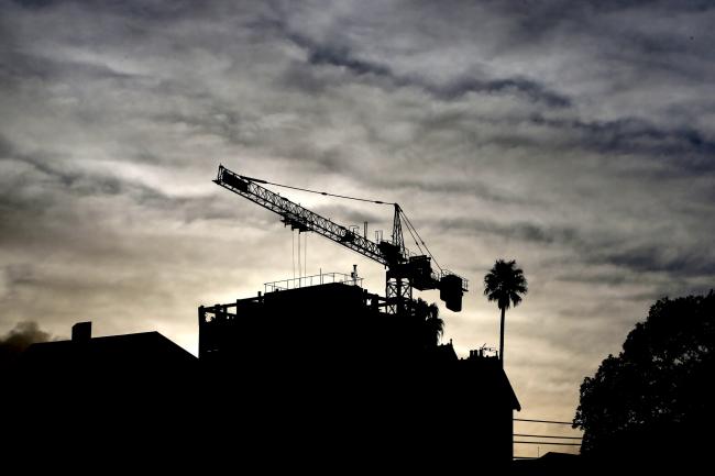 © Bloomberg. A crane is silhouetted as it operates at a residential construction site in the suburb of North Sydney in Sydney, Australia, on Wednesday, June 20, 2018. Australia is riding out a huge gamble on property. The bet: 27 years of recession-free economic growth—during which Sydney home prices surged fivefold—would continue unabated and allow borrowers to keep servicing their debt. 