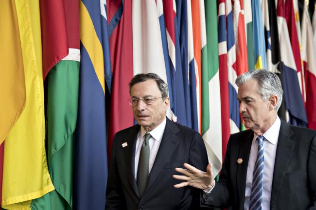 © Bloomberg. Jerome Powell, chairman of the U.S. Federal Reserve, right, walks with Mario Draghi, president of the European Central Bank (ECB), during the spring meetings of the International Monetary Fund (IMF) and World Bank in Washington, D.C., U.S., on Friday, April 20, 2018. The IMF said this week the world's debt load has ballooned to a record $164 trillion, a trend that could make it harder for countries to respond to the next recession and pay off debts if financing conditions tighten. 