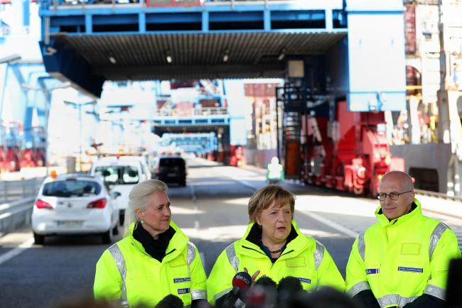 © Bloomberg. Angela Merkel, Germany's chancellor, center, speaks to members of the media as Angela Titzrath, chair of Hamburger Hafen Und Logistik (HHLA), left, and Peter Tschentscher, Hamburg's mayor, stand during a visit to the HHLA Container Terminal Altenwerder (CTA) in the port of Hamburg in Hamburg, Germany, on Monday, May 6, 2019. Merkel said Germany needs to stand up for multilateral agreements and strengthening the World Trade Organization in the face of recent “protectionist tendencies.” Photographer: Krisztian Bocsi/Bloomberg