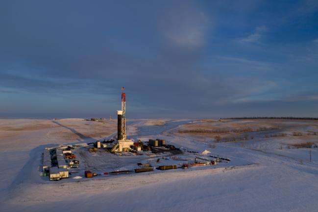 © Bloomberg. An American flag flies on top of a Unit Drilling Co. rig in the Bakken Formation in this aerial photograph taken outside Watford City, North Dakota, U.S., on Friday, March 9, 2018. When oil sold for $100 a barrel, many oil towns dotting the nation's shale basins grew faster than its infrastructure and services could handle. Since 2015, as oil prices floundered, Williston has added new roads, including a truck route around the city, two new fire stations, expanded the landfill, opened a new waste water treatment plant and started work on an airport relocation and expansion project. Photographer: Daniel Acker/Bloomberg
