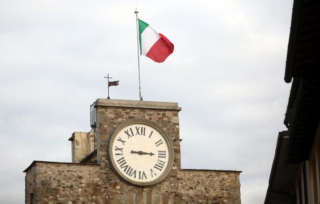 © Bloomberg. The Italian national flag flies atop a clock tower. Photographer: Chris Ratcliffe/Bloomberg