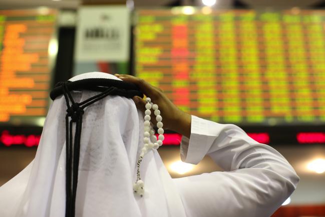 © Bloomberg. A visitor holds prayer beads while looking at financial information screens at the Dubai Financial Market (DFM) in Dubai, United Arab Emirates. Photographer: Jasper Juinen/Bloomberg