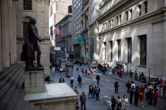 © Bloomberg. Pedestrians walk along Wall Street near the New York Stock Exchange (NYSE) in New York, U.S., on Friday, May 24, 2019. U.S. equities climbed at the end of a bruising week in which escalating trade tensions dominated markets. 