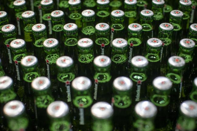 © Bloomberg. Lids sit on green Heineken beer bottles moving along a conveyor at the Heineken NV brewery in Zoeterwoude, Netherlands, on Wednesday, May 30, 2018. Heineken has acquired Stellenbrau, a beer maker based in South Africa's western Cape, submitted a bid for a local Coca-Cola bottler and built a brewery in Ivory Coast to take on market leader Castel. 