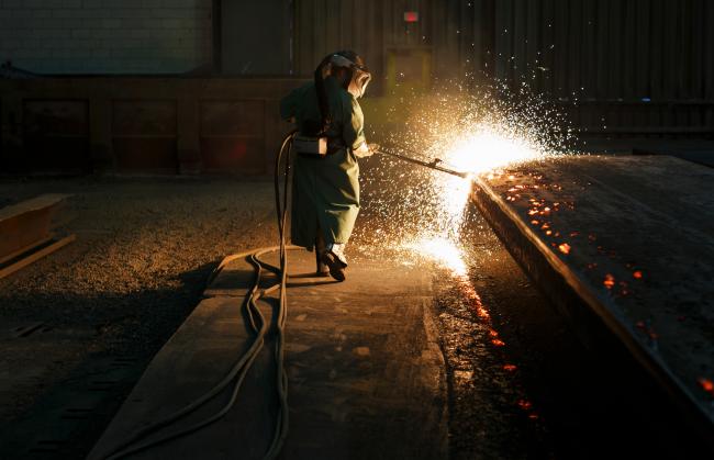 © Bloomberg. Sparks fly as an employee performs a quality check on a steel slab at a plant in Nanticoke, Ontario, Canada. 