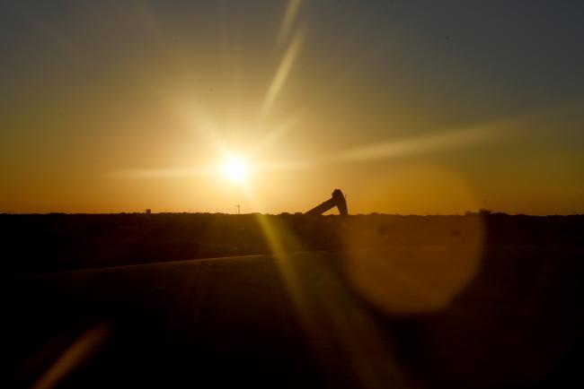 © Bloomberg. The sun sets behind an oil rig seen from Monahans Sandhills State Park in Monahans, Texas, U.S., on Tuesday, June 19, 2018. In the West Texas plains, frack-sand mines suddenly seem to be popping up everywhere. Twelve months ago, none of them existed - together, these mines will ship some 22 million tons of sand this year to shale drillers in the Permian Basin, the hottest oil patch on Earth. Photographer: Callaghan O'Hare/Bloomberg