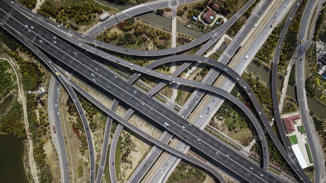 © Bloomberg. Vehicles travel along highways in this aerial photograph taken above Shanghai, China, on Monday, April 2, 2018. China's sprawling local government financing system needs 