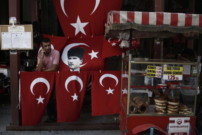 © Bloomberg. A man uses a mobile phone beside a street vendor's display of Turkish flags and an image of Kemal Ataturk, founder of the Turkish republic, in the Sultanahmet district of Istanbul, Turkey, on Thursday, Aug. 3, 2017. Turkey’s central bank raised its inflation forecast for this year on higher food prices, and reiterated its policy not to loosen monetary conditions until the outlook improves. Photographer: Kostas Tsironis/Bloomberg