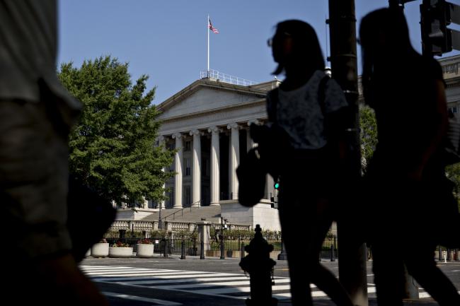 © Bloomberg. Pedestrians walk near the U.S. Treasury building in Washington, D.C., U.S., on Monday, July 16, 2018. The House this week plans to consider a minibus spending bill that combines legislation funding the Treasury, Internal Revenue Service (IRS), and the Securities and Exchange Commission (SEC) with another bill keeping the Interior Department and Environmental Protection Agency (EPA) running. Photographer: Andrew Harrer/Bloomberg