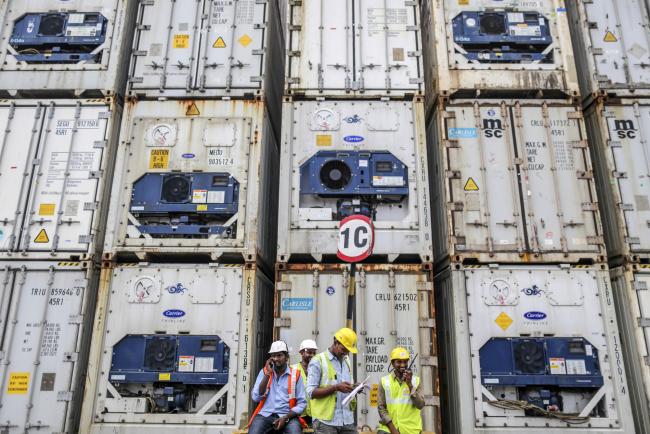 © Bloomberg. Workers sit in front of containers stacked in a yard at Krishnapatnam Port in Krishnapatnam, Andhra Pradesh, India, on Monday, Aug. 11, 2017. Growth in gross domestic product slipped to a three-year low in the April-June quarter, muddying the near-term outlook, though the goods and services tax, or GST, is expected to boost productivity in the longer term.