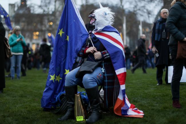 © Bloomberg. An anti-Brexit demonstrator wearing a unicorn mask sits outside of the Houses of Parliament in London, U.K., on Tuesday, Jan. 15, 2019. U.K. Prime Minister Theresa May is set to see her Brexit deal rejected in the biggest Parliamentary defeat for a British government in 95 years after her last minute pleas for support appeared to fall on deaf ears. Photographer: Simon Dawson/Bloomberg
