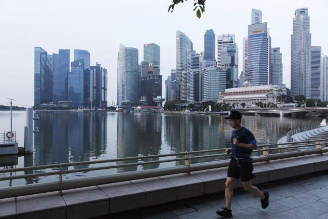 © Bloomberg. A man runs along a promenade past commercial buildings standing in the central business district in Singapore, on Friday, Feb. 16, 2018. Singapore’s dollar is little changed near a three-week high amid thin trading with many Asian markets closed for Lunar New Year holidays. The central bank will announce the amount of 30-year bonds to be auctioned next week in the only planned sale of this tenor in 2018.