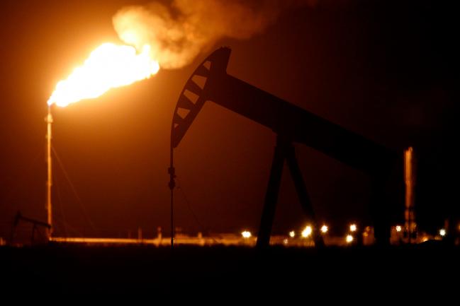 © Bloomberg. The silhouette of an electric oil pump jack is seen near a flare at night in the oil fields surrounding Midland, Texas, U.S.