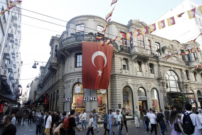 © Bloomberg. Pedestrians walk past a Forever 21 Inc. store decorated with a large Turkish national flag on Istiklal street in Istanbul, Turkey, on Friday, July 6, 2018. Recep Tayyip Erdogan, Turkey's longest-serving ruler since the Republic was founded in 1923, won a five-year term on June 24, securing a mandate to rule with greater executive powers. He has already governed three times as prime minister and served one term as president. 